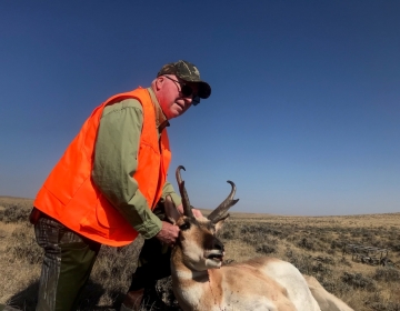 A hunter posing in his fluorescent orange vest with his pronghorn antelope