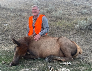 A proud SNS hunter poses with a successful cow elk harvest in Wyoming's scenic plains, showcasing a rewarding hunt experience.