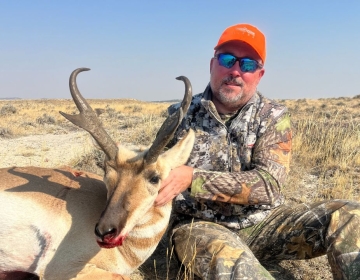 An SNS guide smiles alongside a harvested Wyoming pronghorn buck with impressive horns, a testament to a successful pronghorn hunt in the open terrain.