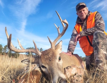 Hunter in an orange vest posing in prairie grass with his 9 point whitetail deer