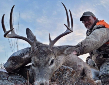 Hunter posing with his whitetail deer laying on limestone rocks after a Wyoming hunt