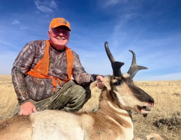 Hunter smiling with a harvested pronghorn antelope in a sunny open field, showing the excitement of a Wyoming hunting experience.