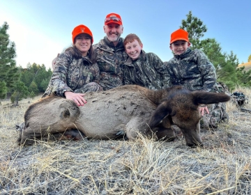 A family poses together after their successful hunt, featuring a cow elk, showcasing a memorable outing with SNS Outfitter & Guides in Wyoming.