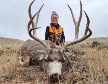 Female hunter in orange safety gear with a 5x5 mule deer buck, emphasizing a memorable guided hunting experience in Wyoming.