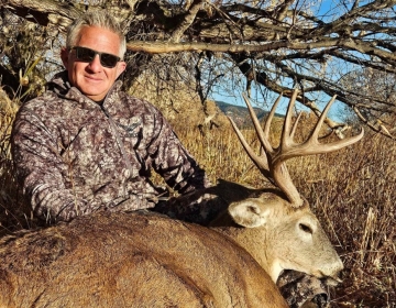 Hunter wearing camouflage sitting beside a large trophy whitetail buck during a successful guided hunt in Wyoming.